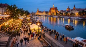 A vibrant, high-angle evening shot of the illuminated Oder river embankments in Wrocław, featuring g